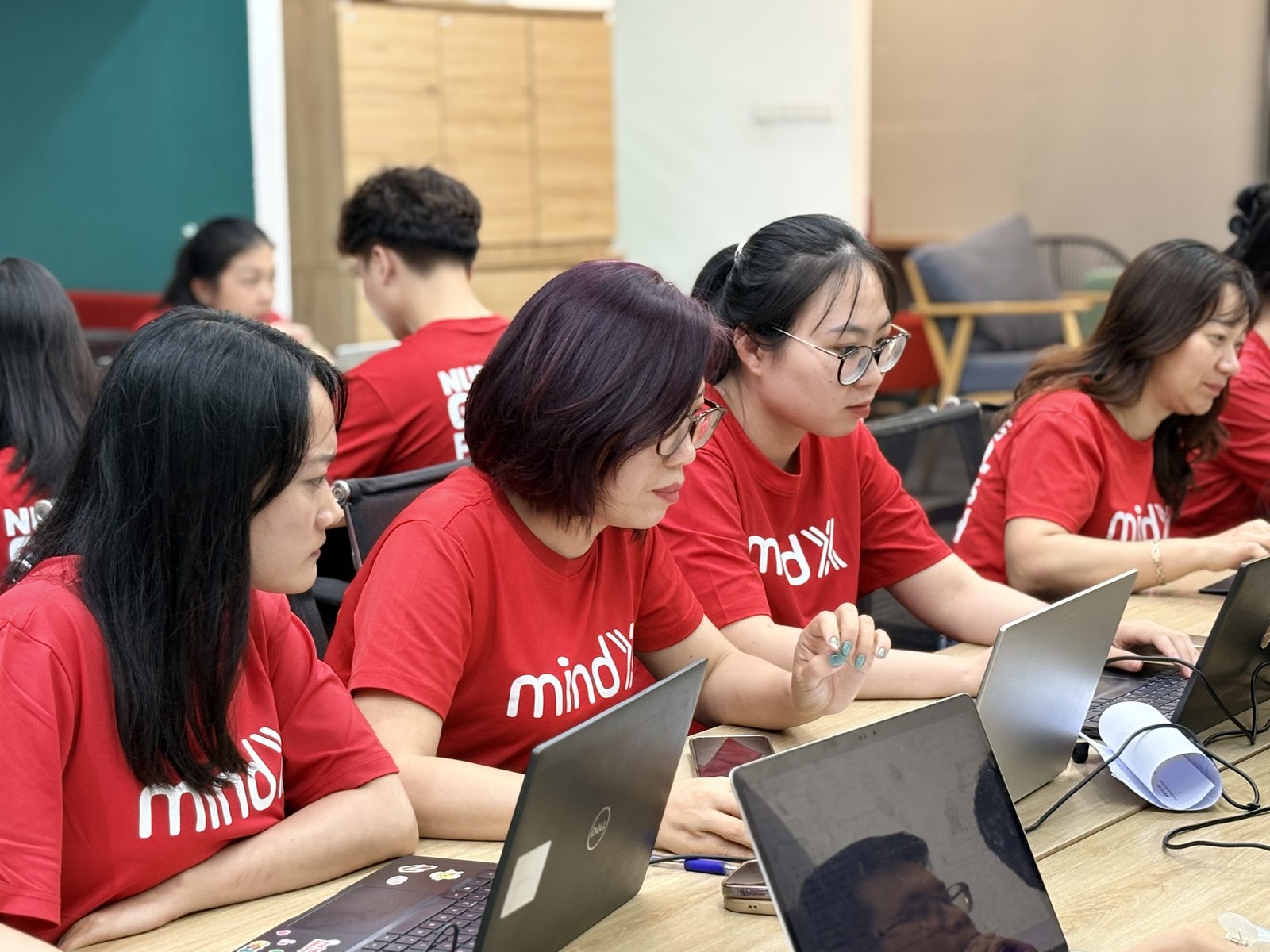 Các MindXers mặc áo đồng phục đỏ ngồi sát nhau, mỗi người chăm chú thao tác trên laptop của mình